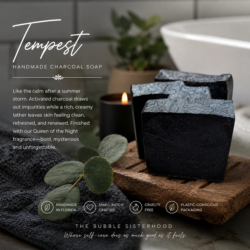 Three dark charcoal handcrafted soap bars labeled Tempest, displayed on a wooden board with a towel, eucalyptus leaves, and a candle in a bathroom setting.