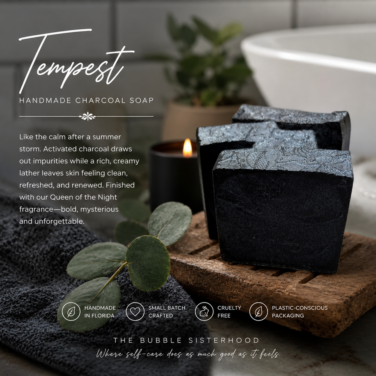 Three dark charcoal handcrafted soap bars labeled Tempest, displayed on a wooden board with a towel, eucalyptus leaves, and a candle in a bathroom setting.
